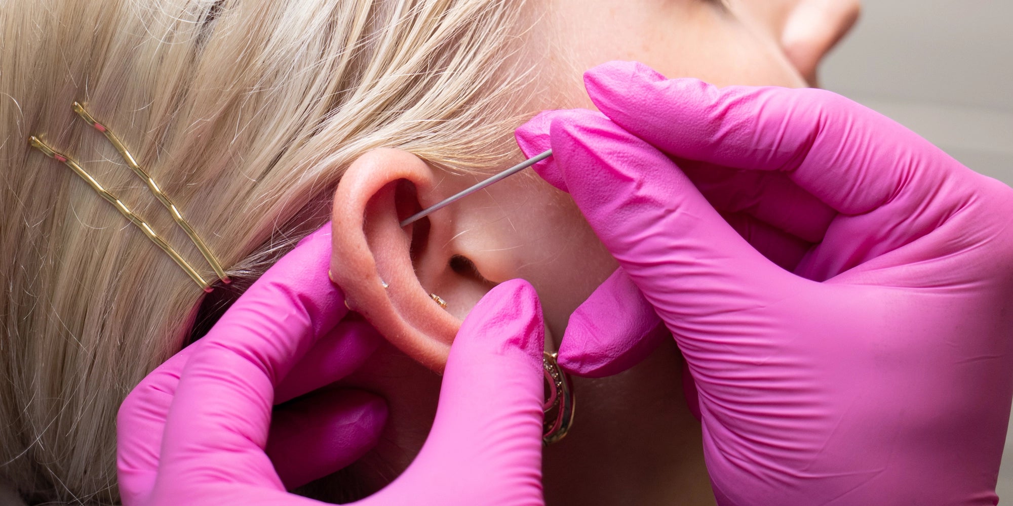 pink gloved piercing an ear